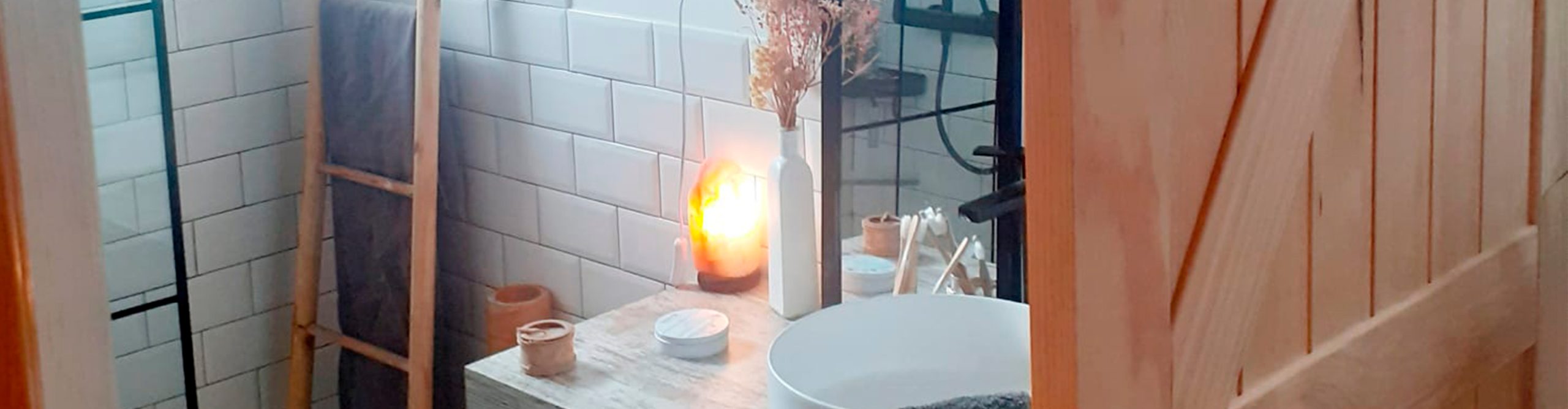 Detalle de un baño moderno con lavabo de cerámica, mueble de madera y decoración con luz cálida.